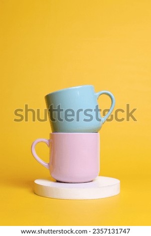 Minimal composition of ceramic mugs stacked on round shaped podium against yellow background