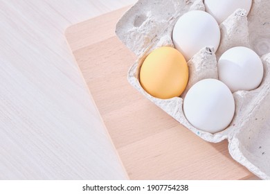 Minimal concept Easter. one colored egg and several white eggs in a cardboard box and a wooden cutting board on the table