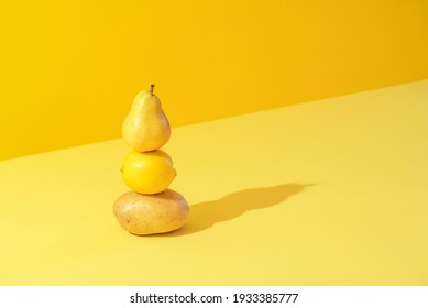 Minimal concept with potato, lemon, and a pear stacked on a yellow background in bright light. Yellow monotone image with vegetables and fruits.