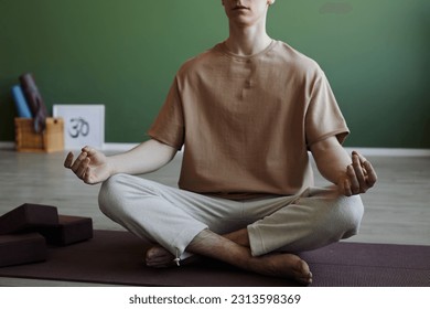 Minimal cropped shot of blissful young man meditating indoors sitting in lotus position, copy space - Powered by Shutterstock