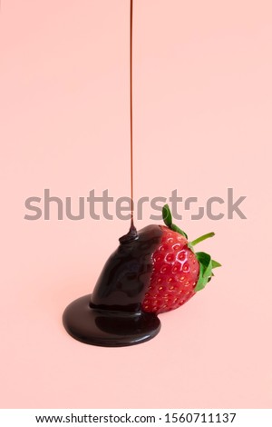 Minimal dark chocolate pouring drop to red strawberries on pastel pink background