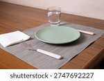 Minimal dining table setting for one person with plate, fork, knife, napkin and glass of water. Concept of simple meal, portion control, healthy lifestyle or living alone.