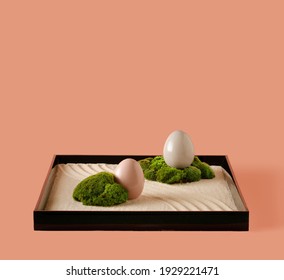 Minimal Easter Holiday Concept Zen Garden Box With Raked Beige Sand, Moss Egg Nest With Pastel Pink And Grey Eggs On Pastel Pink Background.Creative Copy Space.