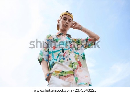 Minimal fashion portrait of young Asian man looking at camera wearing trendy outfit against clear blue sky, copy space