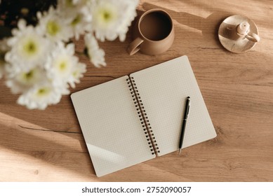 Minimal flat lay of an open grid notebook, coffee cup, and white chrysanthemum bouquet on a table, perfect for mindfulness, morning routine, work, study and cozy home lifestyle.