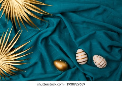 Minimal flat lay view of Easter eggs and golden palm leaves against blue or cyan fabric background. - Shutterstock ID 1938929689