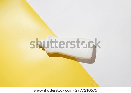 Minimal flat lay of a white plastic detergent bottle on a vibrant yellow and white split background. Strong lighting creates a defined shadow, adding depth and contrast. Modern, eye-catching composition ideal for cleaning, household products, and commercial design use.