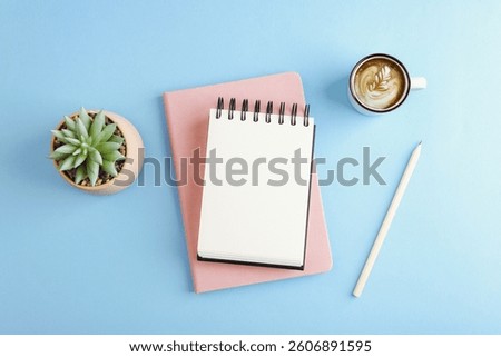 Minimal flat lay of workspace with notebook, coffee cup, pencil and succulent on blue pastel background. Top view, mockup.