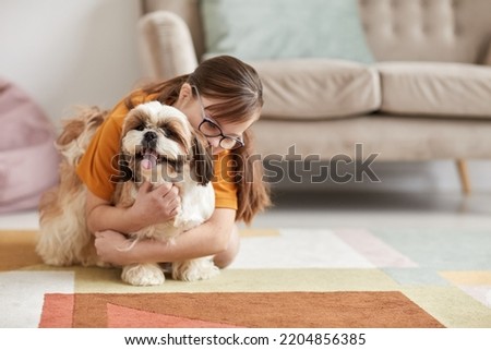 Minimal full length portrait of teenage girl with Down syndrome playing with dog on floor in cozy home interior, copy space