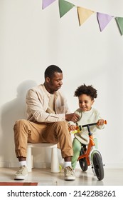 Minimal Full Length Portrait Of Young Black Father Teaching Little Boy Riding Balance Bike At Home