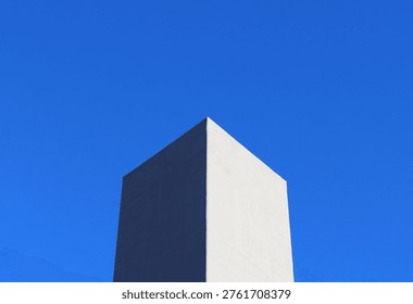 Minimal geometric architecture with sharp cube corner against clear blue sky. Clean composition with strong contrast, light and shadow, and modern abstract aesthetic.