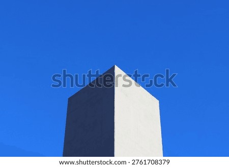 Minimal geometric architecture with sharp cube corner against clear blue sky. Clean composition with strong contrast, light and shadow, and modern abstract aesthetic.