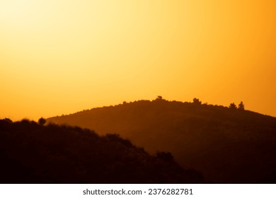 Minimal landscape of two hills at sunsrise with strong orange and yellow light and some fog 