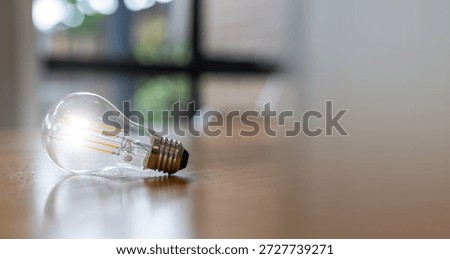 Minimal LED light bulb lying on wooden floor with soft warm glow. Concept of idea, creativity, innovation, energy efficiency, and modern lighting design with copy space for text.