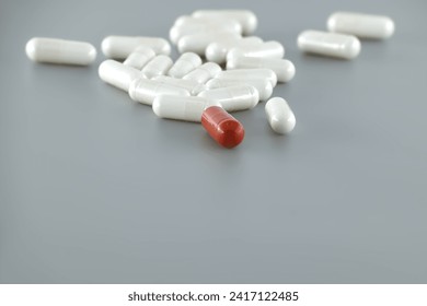 Minimal medical, pharmaceutical concept with white pills scattered on gray surface and single red pill drawing focus, symbolically representing uniqueness or distinction