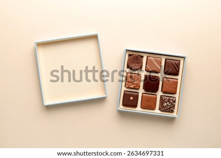 Minimal overhead shot of open box with chocolate squares on beige background, elegant candy dessert packaging concept