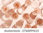 Minimal pattern of Top view glasses of rose wine or champagne on soft pink background, artistic shadows and sun glare. Aesthetic still life Clear crystal wineglass, sparkling drinks for summer party