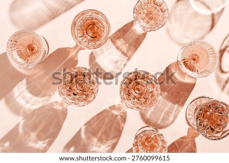 Minimal pattern of Top view glasses of rose wine or champagne on soft pink background, artistic shadows and sun glare. Aesthetic still life Clear crystal wineglass, sparkling drinks for summer party