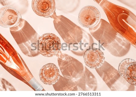 Minimal pattern from wine bottle and glasses of rose wine or champagne on pink with shadows and light reflections. Bright shiny wineglass with sparkling alcohol drink at sunlight, aesthetic flat lay