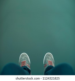 Minimal picture some legs with green sneakers over a green abyss, background, water, environment.	
