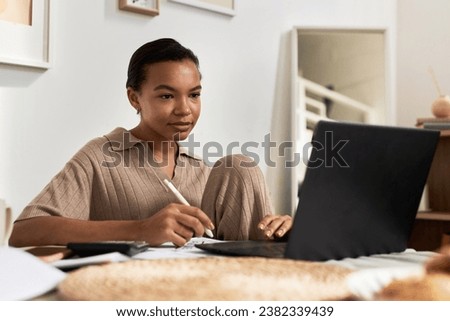 Minimal portrait of Black young woman using laptop while working or studying at home, copy space