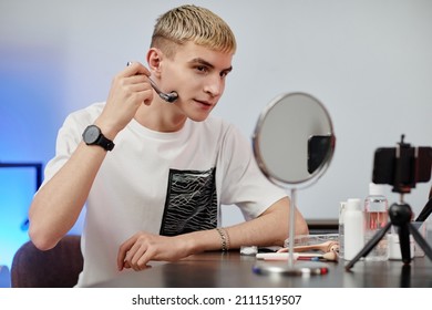 Minimal Portrait Of Blonde Young Man Using Face Massager While Filming Male Skincare Tutorial In Studio