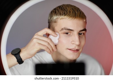 Minimal Portrait Of Blonde Young Man Using Face Massager While Filming Male Skincare Tutorial With Ring Light