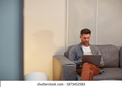 Minimal Portrait Of Handsome Mature Man Working With Laptop While Sitting On Sofa In Minimal Office Interior, Copy Space