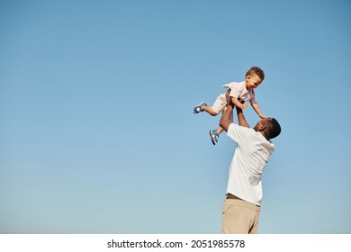 Minimal portrait of happy African-American father playing with cute baby and throwing him against blue sky, copy space - Powered by Shutterstock