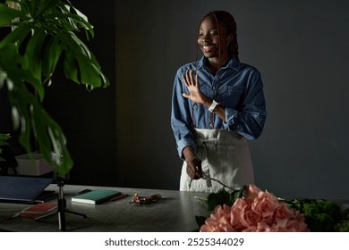 Minimal portrait of young African American woman as florist creating bouquet and filming process with smartphone for social media waving at camera copy space - Powered by Shutterstock