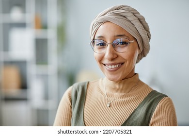 Minimal portrait of young Middle Eastern woman smiling at camera in office setting and wearing headwrap, copy space - Powered by Shutterstock