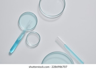 Minimal scene with some glass petri dishes decorated with test tubes filled with blue fluid on white background. Empty area for product display, copy space