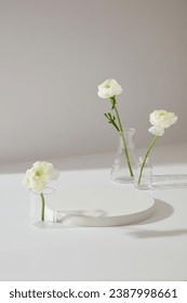 Minimal scene of white background featured few Persian Buttercup flowers inside glassware. Blank round podium to display your cosmetic product or goods