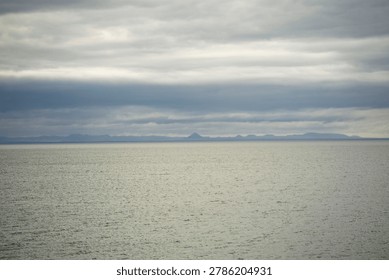 Minimal seascape with distant mountains and dramatic cloudy sky over calm ocean in Iceland