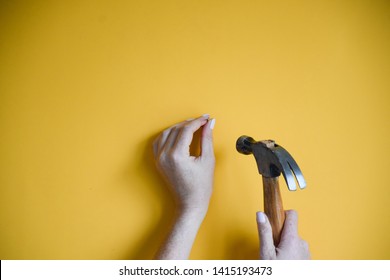 Minimal shot of woman’s hands using a hammer to drive a nail into a yellow wall