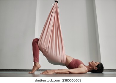 Minimal side view of mature woman enjoying aerial yoga and exercising with pink hammock, copy space - Powered by Shutterstock