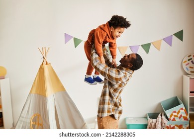 Minimal Side View Portrait Of Loving Black Father Playing With Toddler Son At Home And Holding Him Up In Air, Copy Space