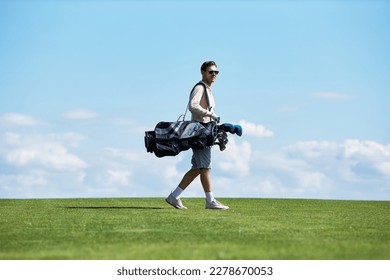 Minimal side view portrait of rich sporty man carrying golf bag walking on green field against sky, copy space - Powered by Shutterstock