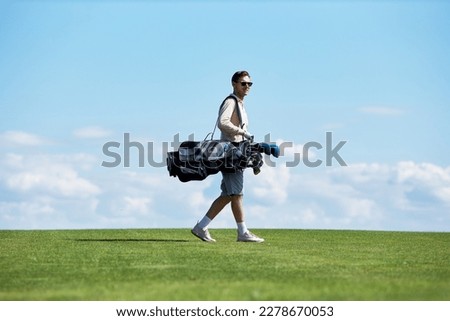 Minimal side view portrait of rich sporty man carrying golf bag walking on green field against sky, copy space