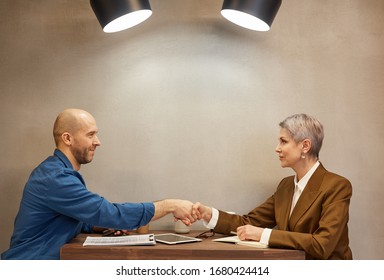 Minimal Side View Portrait Of Two People Shaking Hands While Sitting Across Table In Indoor Cafe During Business Meeting, Copy Space