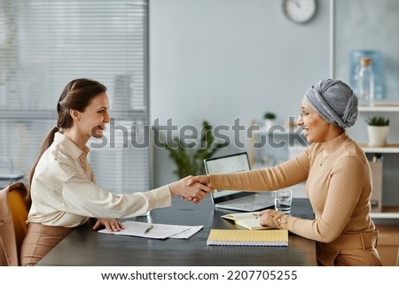 Minimal side view portrait of two female entrepreneurs shaking hands over meeting table in office