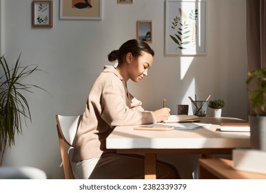 Minimal side view portrait of young African American woman writing in notebook at home with sun rays, copy space