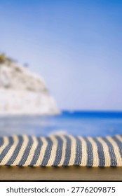Minimal summer composition featuring clean sandy beach with empty copy space for product placement. In the background, a rocky coastline meets the sea under a bright blue sky, creating a natural and scenic atmosphere. Ideal for advertising, travel promotions, and summer lifestyle concepts.