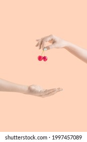 Minimal Summer Fruit Composition With A Hand Giving A Red Organic Cherry On Bright Orange Background. Sharing Food And End Hunger Idea. Creative Healthy Diet Concept Aesthetic.