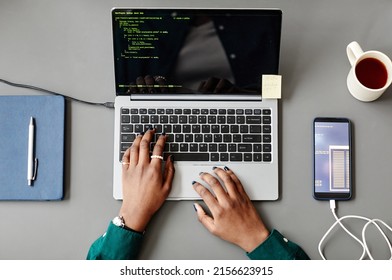 Minimal top view of unrecognizable black woman using laptop and writing code at grey workplace desk
