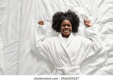 Minimal top view of young Black woman falling onto bed enjoying relaxing SPA vacation in hotel and smiling at camera, copy space