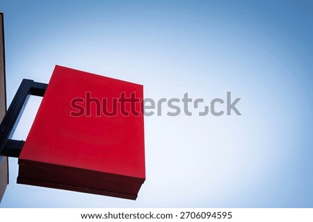 Minimal view of a blank rectangular red sign mounted on a bracket against a clear blue sky. The empty panel offers copy space for branding, advertising, or wayfinding in a clean, modern urban setting.