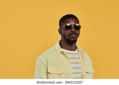 Minimal Waist Up Portrait Of Trendy African-American Man Wearing Sunglasses And Looking At Camera While Standing Against Yellow Background In Studio, Copy Space