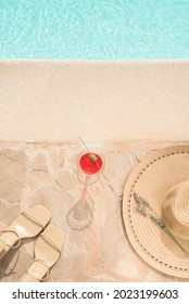 Minimal Warm Aesthetic Summer Vacation Concept Background With Swimming Pool. Straw Hat, Sandals And A Cocktail On A Stone Swimming Pool Side, Clear Blue Water With Waves, Sunlight Shadow Reflections