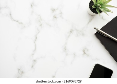 Minimal white marble office desk table with office supplies and smartphone. Top view with copy space, flat lay. 